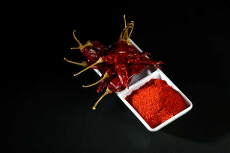 chilly powder with red chilly in white plate, dried chillies on black backgroundの写真素材