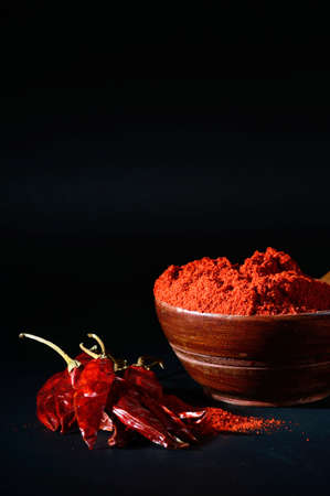 chilly powder in wooden bowl with red chilly, dried chillies on black backgroundの写真素材