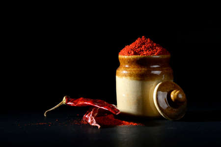 Red Chili Pepper powder in clay pot with Red Chili Peppers on black backgroundの写真素材