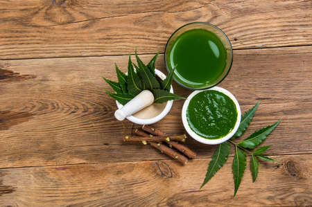 Medicinal Neem leaves in mortar and pestle with neem paste, juice and twigs on wooden backgroundの写真素材