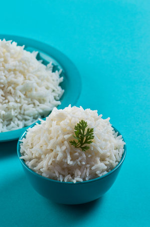 Cooked plain white basmati rice in a blue plate and bowl on blue backgroundの写真素材