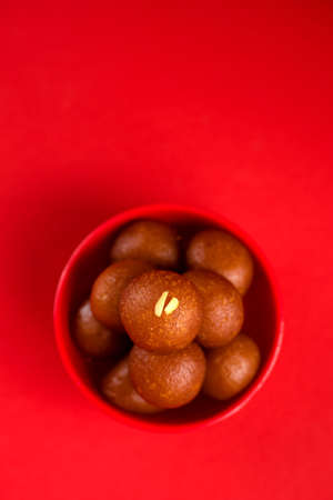 Gulab Jamun in red bowl on red background. Indian Dessert or Sweet Dish.の写真素材