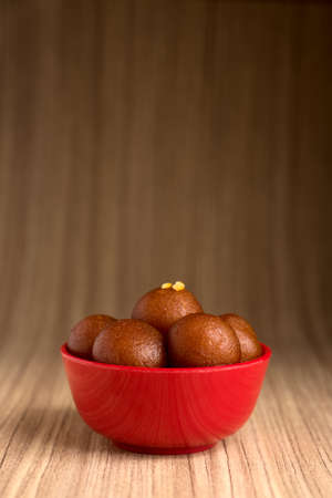 Gulab Jamun in red bowl on wooden background. Indian Dessert or Sweet Dish.の写真素材