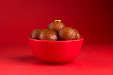 Gulab Jamun in red bowl on red background. Indian Dessert or Sweet Dish.の写真素材