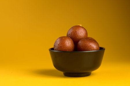 Indian Dessert or Sweet Dish : Gulab Jamun in bowl on yellow background.
