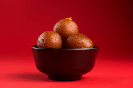Gulab Jamun in black bowl on red background. Indian Dessert or Sweet Dish.の写真素材