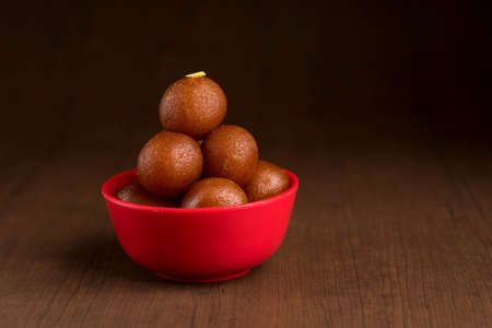 Gulab Jamun in red bowl on wooden background. Indian Dessert or Sweet Dish.の写真素材