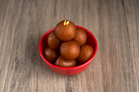 Gulab Jamun in red bowl on wooden background. Indian Dessert or Sweet Dish.
