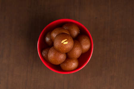Gulab Jamun in red bowl on wooden background. Indian Dessert or Sweet Dish.の写真素材