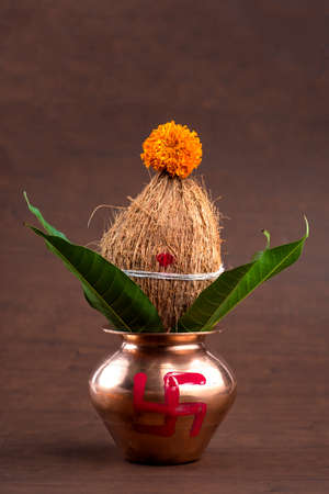 Copper kalash with coconut and mango leaf with floral decoration on a wooden background. essential in hindu puja.の写真素材