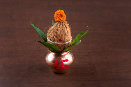 Copper kalash with coconut and mango leaf with floral decoration on a wooden background. essential in hindu puja.の写真素材