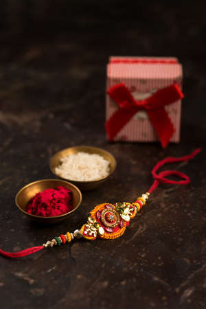 Raksha Bandhan background with an elegant Rakhi, Rice Grains, Kumkum and gift box. A traditional Indian wrist band which is a symbol of love between Brothers and Sisters.の写真素材