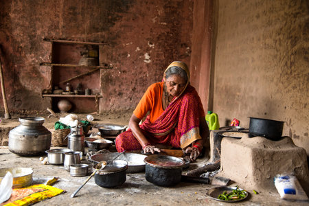 CHIKHALDARA, MAHARASHTRA - AUGUST 28, 2018: An Unidentified old woman making and cooking / baking fresh food in a rural village in a vintage kitchen using firewood in earthen chulhas.のeditorial素材