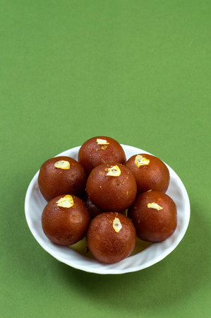 Gulab Jamun, Indian dessert topped with pistachio in white plate on green backgroundの写真素材