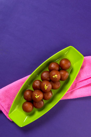 Indian Dessert Gulab Jamun in plate on purple background with napkin