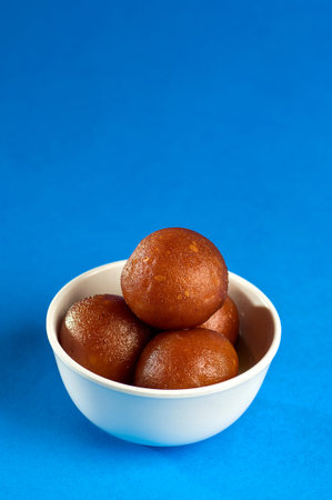 Indian Dessert : Gulab Jamun in bowl with spoon on blue background