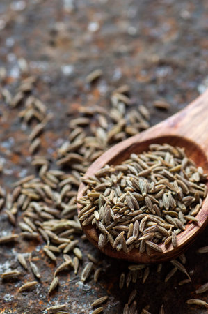 Cumin seeds in wooden spoon on a textured background