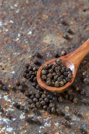 Peppercorns in wooden spoon on texture background