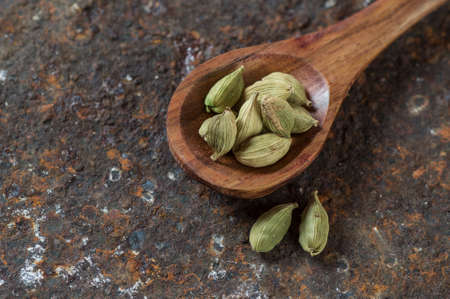 Cardamom pods in wooden spoon on a textured backgroundの写真素材