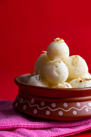 Indian Sweet or Dessert - Rasgulla, Famous Bengali sweet in clay bowl with napkin on Red Background