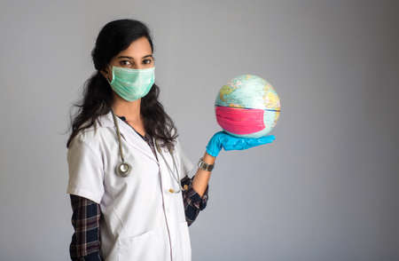 Woman doctor holding world globe with a medicine face mask. World epidemic of coronavirus concept.の写真素材