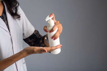 Portrait of woman doctor using a sanitizing gel from a bottle for hands cleaning.の写真素材