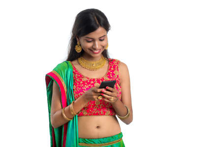 Young Indian traditional girl using a mobile phone or smartphone isolated on a white backgroundの写真素材