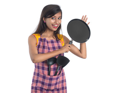 Young Indian woman holding kitchen utensil (spoon, stapula, ladle, and pan, etc.) on a white backgroundの写真素材