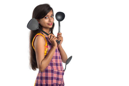 Young Indian woman holding kitchen utensil (spoon, stapula, ladle, and pan, etc.) on a white backgroundの写真素材