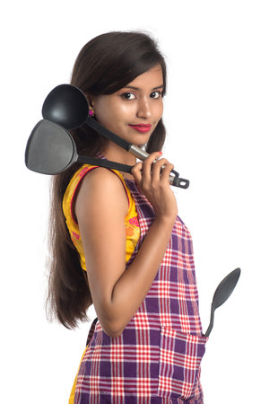 Young Indian woman holding kitchen utensil (spoon, stapula, ladle, and pan, etc.) on a white backgroundの写真素材