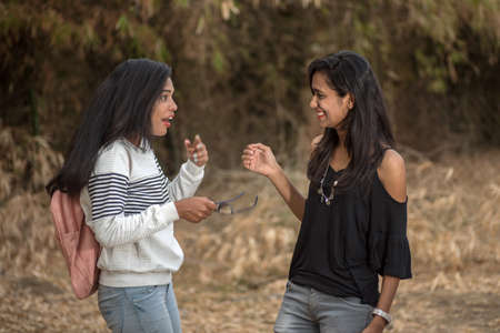 Two young girl friends standing together and having fun in outdoors. Looking at camera.の写真素材