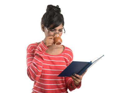 Beautiful young girl with book and cup of coffee posing on a white background.