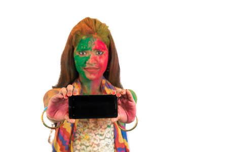 Young girl with colorful face showing smart phone screen on Holi festival. Festival and technology concept on white background.の写真素材