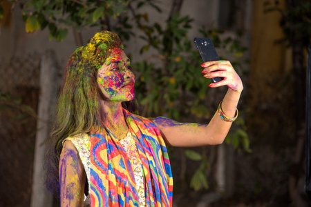 Young girl with colorful face taking selfie using smartphone on Holi festival. Festival and...