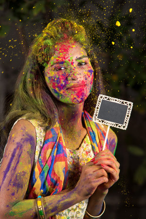 Young girl holding the small board on the occasion of Holi festival with faces painted with powdered colors, with a colour splash.の写真素材