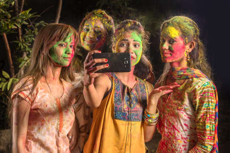 Group of happy young girls having fun and taking selfie using smartphone on Holi festival. Festival and technology conceptの写真素材