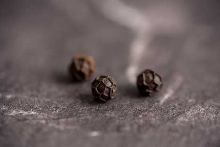 Close up of black pepper or peppercorns on a stone background.