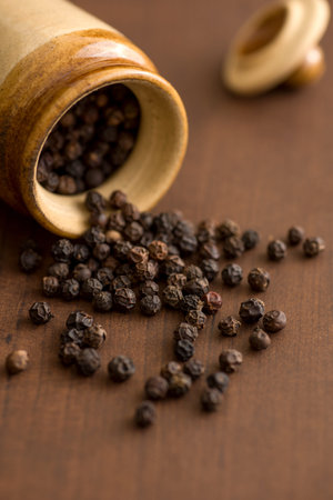 Close up of black pepper or peppercorns with clay pot on a wooden background.