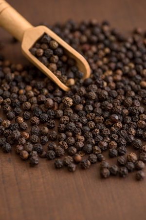Close up of black pepper or peppercorns in wood scoop on a wooden background.