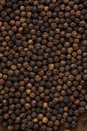 Close up of black pepper or peppercorns as background on wooden background.
