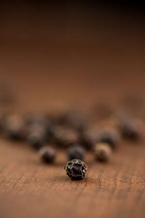 Close up of black pepper or peppercorns on a wooden background.の写真素材