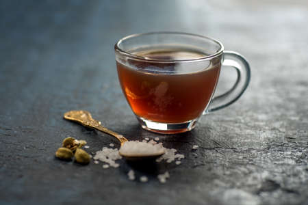 A cup of tea and cardamom with sugar in a spoon on a textured background.の写真素材