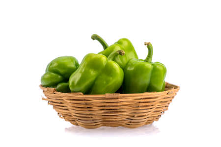 Fresh green bell pepper or capsicum in bamboo basket on a white backgroundの写真素材