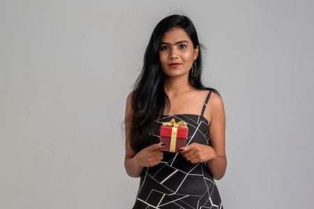Portrait of a pretty young girl posing with gift box on grey background.の写真素材