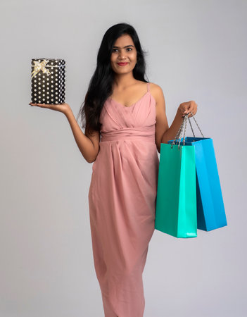 Pretty young girl posing with shopping bag and gift box on a grey backgroundの写真素材