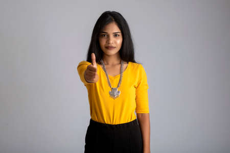 Young smiling girl showing ok sign or thumbs up on a grey backgroundの写真素材