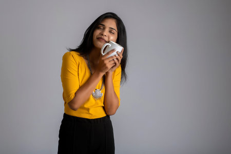 pretty young girl with a cup of tea or coffee posing on grey backgroundの写真素材