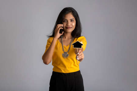 Young Indian girl using mobile phone or smartphone and showing small board on gray background.の写真素材
