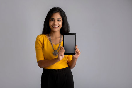 Young beautiful girl holding and showing blank screen of smartphone or mobile or tablet phone on a gray background.の写真素材