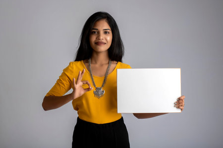 A young girl or businesswoman holding a signboard in her hands on a gray background.の写真素材